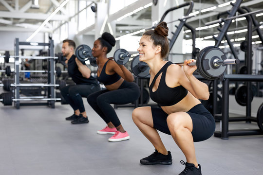 sportive people, multiethnic group perform exercises with heavy weights in gym. young diverse man and women workout, have muscular body