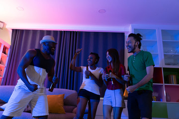 Friends laughing in sofa at home party under colorful light with drink and snack