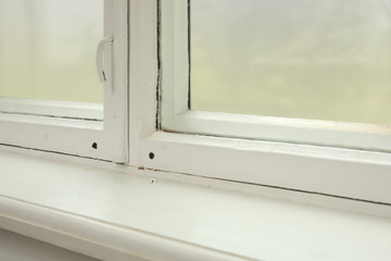 Old window with white wooden sill in room, closeup
