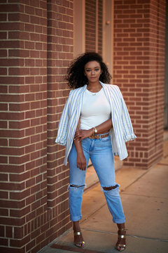 Stunning Young Black Woman Poses Near Brick Wall Wearing Blue Jeans, White Shirt And Blazer - Fashion And Business Casual