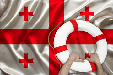 male hands hold on a white life buoy against the background of the silk national flag of Georgia,...