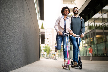 Two smiling business people driving electric scooter going to work.
