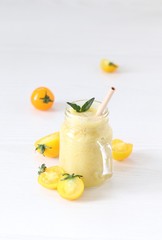 Vegetable smoothie yellow tomato in a glass jar with bamboo straw on a light background
