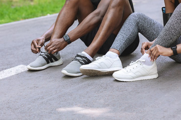 Couple of black runners lace their shoes outdoors, preparing for jogging