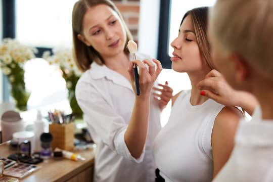 team of professional caucasian makeup artists working with young model. two make-up artist doing make-up in two hands and talk