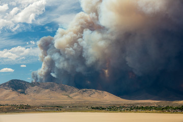 Blue and white sky puffy cumulonimbus clouds and smoke from a large wildfire in the desert muddy lake in foreground