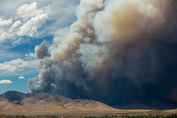 Blue and white sky puffy cumulonimbus clouds and smoke from a large wildfire in the desert