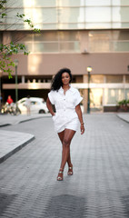 Stunning young black woman poses in city street or alley wearing white romper