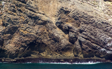 Gorgeous massive cliff with ocean waves crashing its base. Beautiful colors and texture in natural...