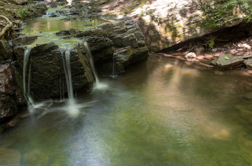 Full frame image of forest waterfall cascading over an ancient rock formation. Water is smooth and reflects forest colors in long exposure shot with copy space.