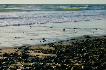 Blue ocean with waves approaching beach of sand and rock
