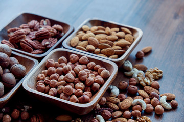 Wooden bowl with mixed nuts on table top view. Healthy food and snack. Walnut, pistachios, almonds, hazelnuts and cashews.