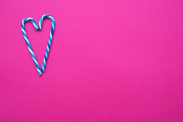 White and blue candy canes in the form of a heart on a pink background, copy space