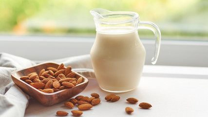 Almond milk in glass with almonds in wooden bowl on a white wooden table