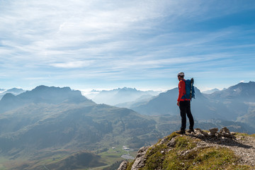 Obraz premium Young mountaineer with helmet stands on the edge and looks into the cloudy distance
