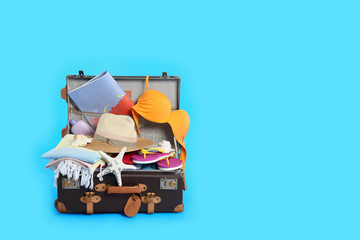 Packed vintage suitcase with different beach objects on light blue background, space for text....