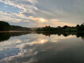 Trees are reflected in the water of the lake. Evening landscape, a small pond in the forest. Reflection of the blue sky and trees in a park reservoir.