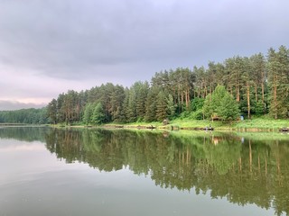 Trees are reflected in the water of the lake. Evening landscape, a small pond in the forest. Reflection of the blue sky and trees in a park reservoir.