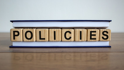 Obraz premium Concept word 'policies' on wooden cubes between pages of a book on a beautiful wooden table. White background. Business concept.