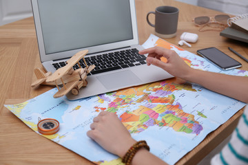 Woman with world map and laptop planning trip at wooden table, closeup