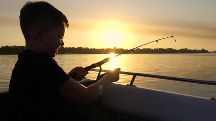 A boy on a fishing trip caught a fish.Fishing on the lake from a boat. Fishing rods in sunlight. Fishing rest concept.	