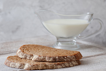 two slices of dark bread, a jug of milk on a wooden table and a gray background in a high key
