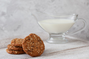 a stack of oatmeal cookies, a jug of milk, cereal on a wooden table and a gray background in a high key