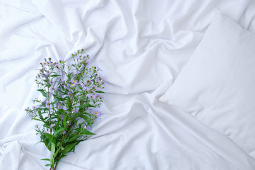 A bouquet of wild flowers on  bed on a white sheet. View from above.