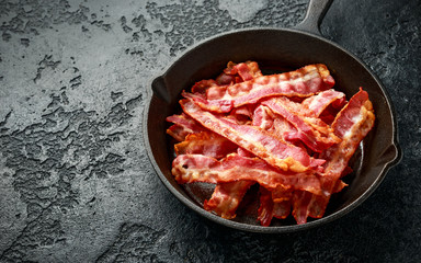 Fried crunchy Streaky Bacon pieces in a cast iron skillet