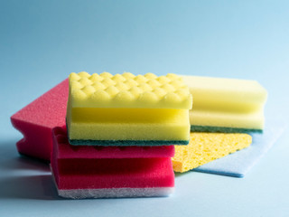 Side view of cleaning sponges of different colors and sizes laid out on a blue background. Home cleaning products