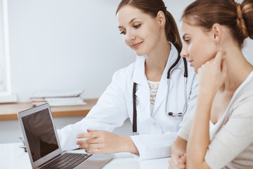 Doctor and patient are sitting and discussing health examination results while using laptop computer. Health care, medicine and good news concepts