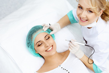 Naklejka premium Professional beautician doing eyebrow tattoo at woman face. Permanent brow makeup in beauty salon, closeup. Cosmetology treatment