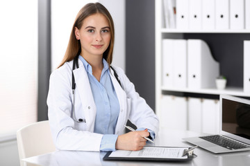 Doctor woman filling up medical form while sitting at the desk in hospital office. Physician at work. Medicine and health care concept