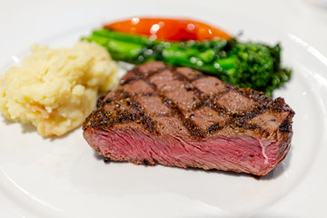 Delicious medium rare sirloin beef steak grilled cut on white dush with mashed potato and vegetables