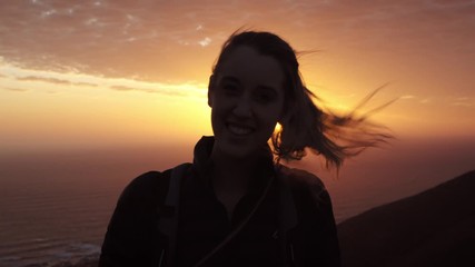 Silhouette of a Young Woman, Smiling to Camera wearing a Rucksack on a Summer Hike.