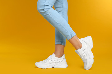 Woman wearing stylish sneakers on yellow background, closeup