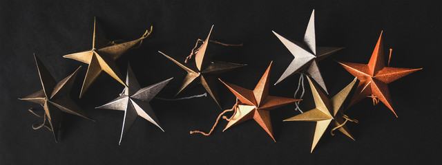 Christmas or New Year holiday texture, wallpaper and background. Flat-lay of paper toy decorative stars over black background, top view, copy space, wide composition. Minimalistic concept