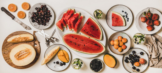 Summer tropical fruit party table. Flat-lay of lunch setting with fruit, berries, watermelon and lemonade over white background, top view. Vegan, vegetarian, clean eating, fruiterian food concept