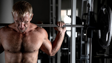 Muscular adult brutal man doing barbell squats in the gym. Portrait of caucasian authentic bodybuilder doing workout exercises
