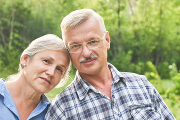 Close-up portrait of elderly couple in love on romantic date in summer park smiling and hugging against the background of green trees