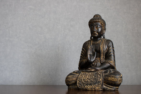 Dusty Buddha statue sitting in meditation on wooden table isolated on clean gray background. Tranquil and minimalist setting with empty space for text