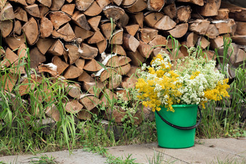 Rustic still life with a bouquet of white and yellow wild flowers in a bucket against the background of a woodpile.