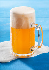 Pint of beer with spilled froth on blue table. German unfiltered beer