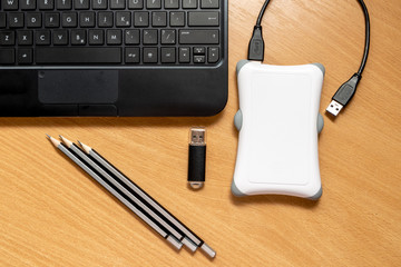 Laptop keyboard. Pencils, flash drive and external hard drive on a wooden table, top view. The...