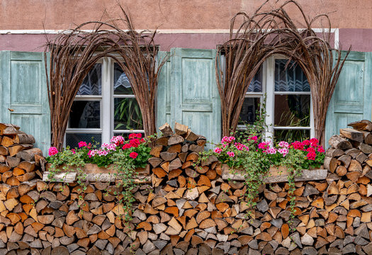 Romantische Fenster-Fassade mit Blumen und Holzscheiten