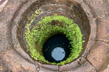 A view into an ancient well with a dark water surface in depth.