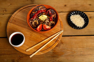 Soba with chicken and vegetables with soy sauce and sesame seeds near the sticks.