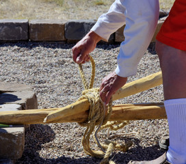 Teepee construction: Craftsman secures teepee poles with rope before the tall logs are erected. © KaeC'sImages