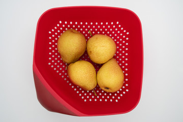 Four ripe pears in red colander