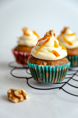 three carrot cake muffin with icing and carrot shaving on cooling rack white background with copy space